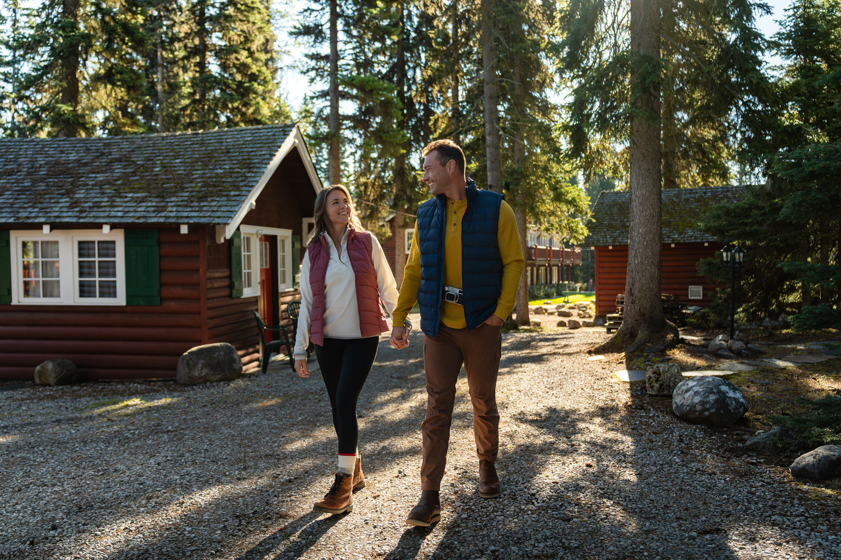 Couple walking among red cabins and pine trees at paradise lodge in lake louise